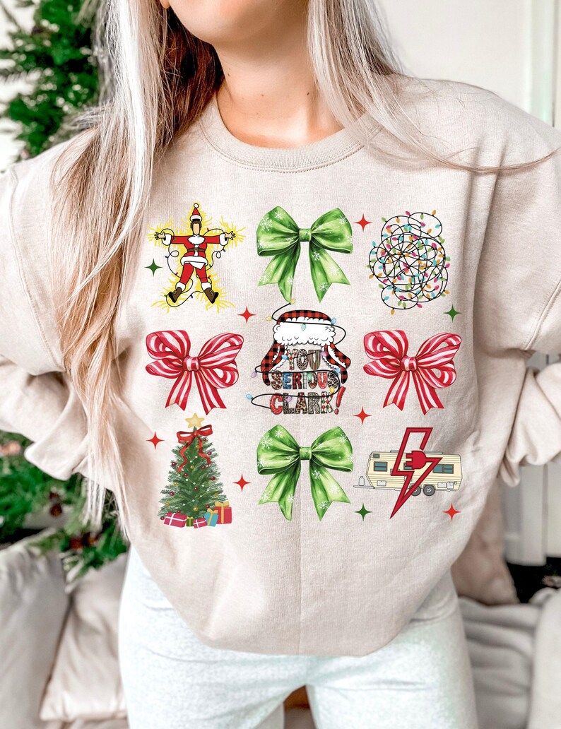 May include: Beige sweatshirt with a festive Christmas-themed design. The design includes images of a Christmas tree, bows, Santa Claus, and a camper with a lightning bolt. Text on the shirt reads "You Serious Clark!"