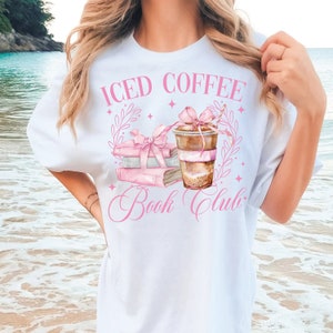 K&ouml;nnte beinhalten: Wei&szlig;es T-Shirt mit einem rosafarbenen Grafikdesign aus einem Stapel B&uuml;cher, einem Glas Eiskaffee und dem Text "Iced Coffee Book Club".