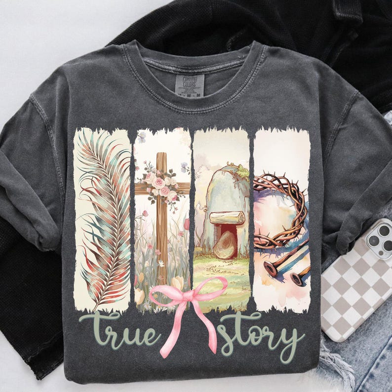Puede incluir: Una camiseta gris antracita con un dise&ntilde;o de acuarela de una rama de palmera, una cruz con flores, una tumba de piedra, una corona de espinas y clavos. El texto "true story" est&aacute; impreso debajo del dise&ntilde;o.