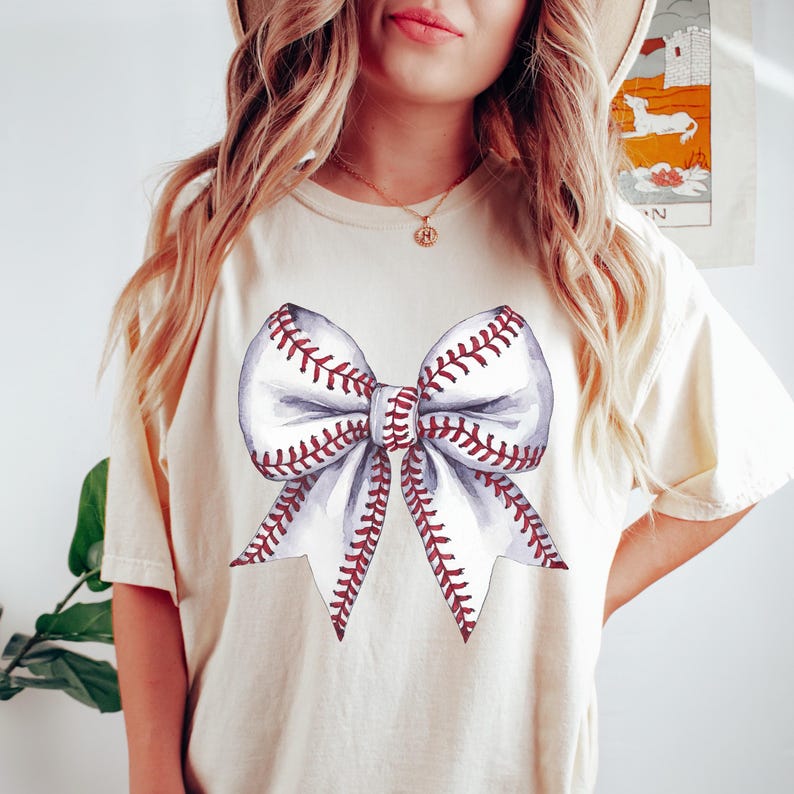Pu&ograve; includere: T-shirt color crema con un design a fiocco ad acquerello. Il fiocco &egrave; progettato per assomigliare a una palla da baseball, con sezioni bianche e cuciture rosse. La maglietta &egrave; uno stile casual e confortevole.