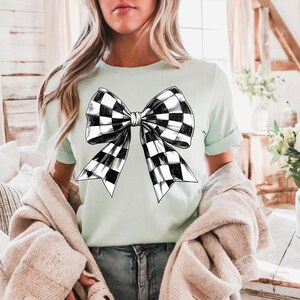 May include: A light green t-shirt featuring a black and white checked bow design.