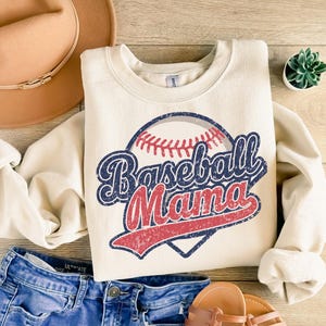 May include: A cream-colored sweatshirt with a vintage-style baseball graphic and the text "Baseball Mama".
