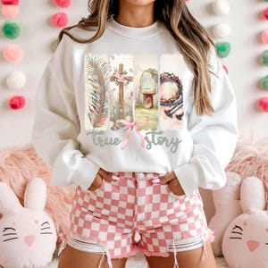 Puede incluir: Sudadera blanca con un gr&aacute;fico de una cruz, una corona de espinas, una tumba y una rama de palma. El gr&aacute;fico est&aacute; rodeado de un efecto acuarela y el texto "true story".