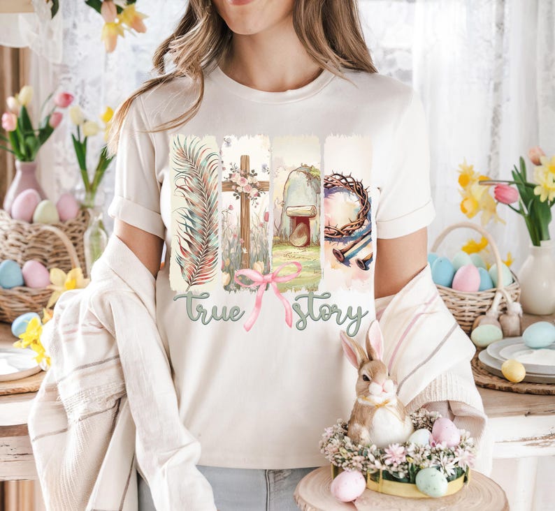 Puede incluir: Una camiseta blanca con un dise&ntilde;o gr&aacute;fico de una cruz, una corona de espinas, una tumba y una hoja de palma. El texto "true story" est&aacute; impreso debajo del gr&aacute;fico.