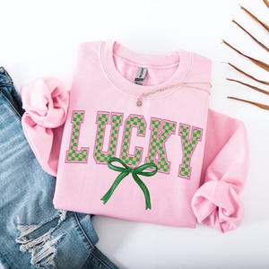 May include: Pink sweatshirt with the word "LUCKY" in green and pink checkered letters with a green bow.