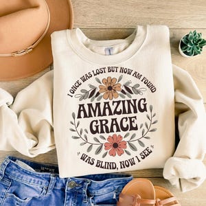 May include: A cream-colored sweatshirt with a floral design and the text "I once was lost but now am found Amazing Grace Was blind, now I see."