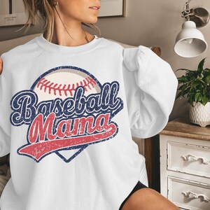 May include: White sweatshirt with a vintage-style baseball graphic and the text "Baseball Mama" in red, blue, and white.