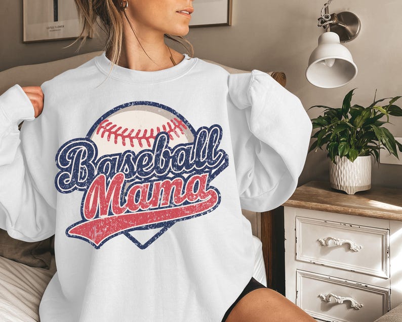 May include: White sweatshirt with a vintage-style baseball graphic and the text "Baseball Mama" in red, blue, and white.