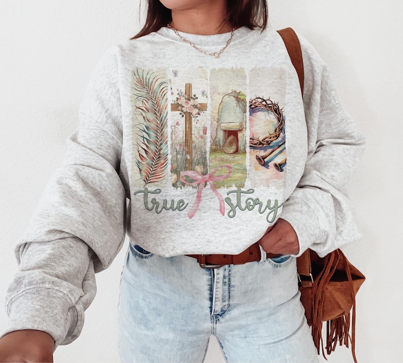 Puede incluir: Una sudadera gris con un estampado gr&aacute;fico de una cruz, una corona de espinas y una tumba. El texto "true story" est&aacute; impreso debajo del gr&aacute;fico.