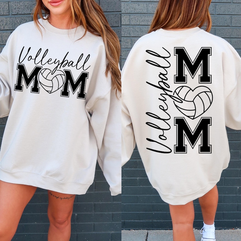 May include: A white sweatshirt with black text that says "Volleyball Mom" on the front and "Volleyball Mom" with a volleyball in a heart on the back.