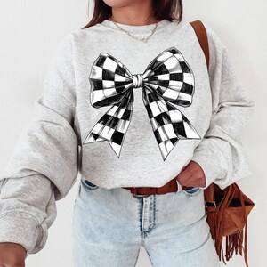May include: A grey sweatshirt featuring a black and white checked bow design.