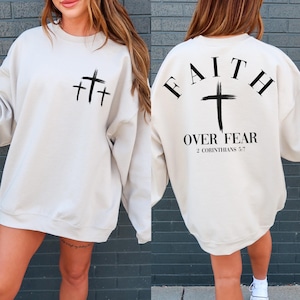 May include: A beige sweatshirt with a black cross design on the front and the text "FAITH OVER FEAR 2 CORINTHIANS 5:7" on the back.