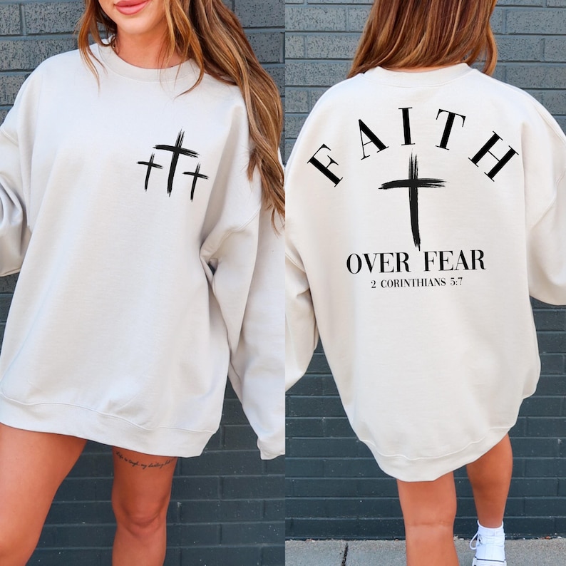 May include: A beige sweatshirt with a black cross design on the front and the text "FAITH OVER FEAR 2 CORINTHIANS 5:7" on the back.
