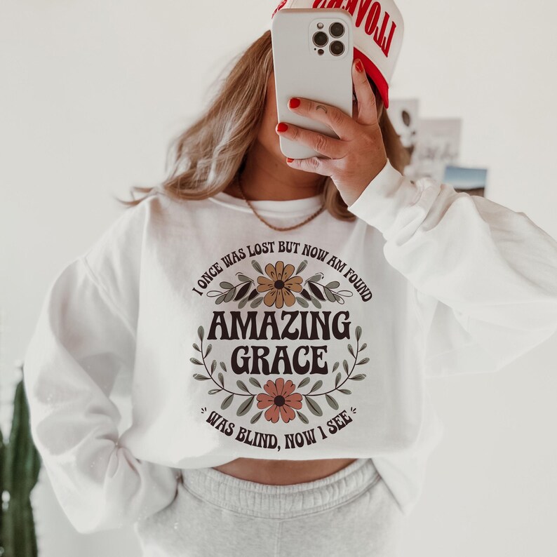 May include: White sweatshirt with a floral design and the text "I once was lost but now am found Amazing Grace Was blind, now I see".