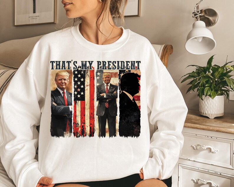 May include: White sweatshirt with a graphic print of three men in front of an American flag. The text "THAT'S MY PRESIDENT" is printed above the graphic.