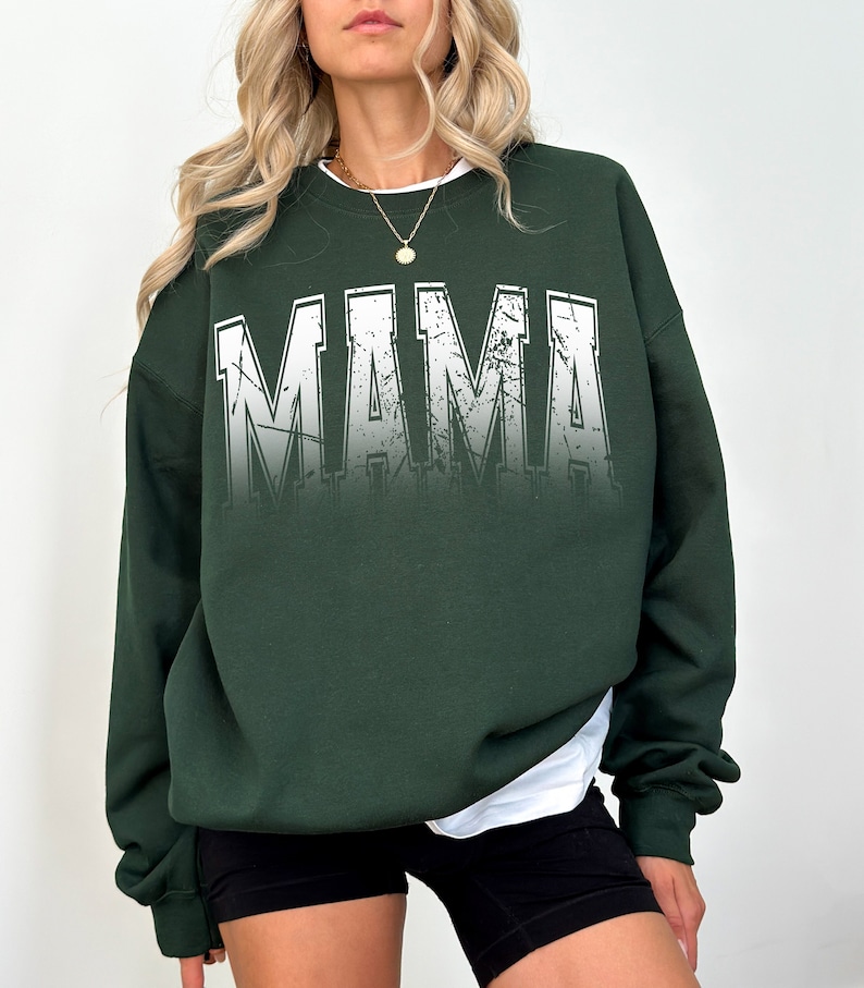 Op de afbeelding: Een donkergroen sweatshirt met het woord "MAMA" bedrukt in wit met een verweerd, verbleekt effect.