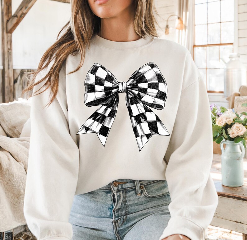 May include: A white sweatshirt featuring a black and white checked bow design.