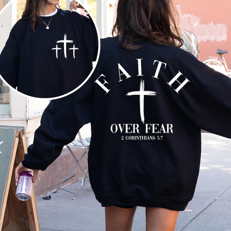 May include: Black sweatshirt with white text that reads "FAITH OVER FEAR 2 CORINTHIANS 5:7" and a white cross. The front of the sweatshirt has three white crosses.
