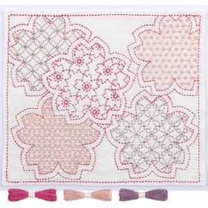 Puede incluir: Un kit de bordado de tela blanca con cuatro madejas de hilo en rosa, rosa claro y morado. La tela tiene un diseño de cinco flores de cerezo rosas y moradas.