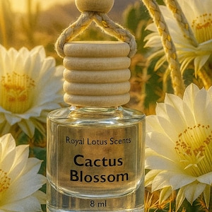 Puede incluir: Una botella de vidrio transparente con tapa de madera y colgador de cuerda, etiquetada como "Royal Lotus Scents Cactus Blossom 8 ml." El fondo presenta flores de cactus blancas y un paisaje desértico.