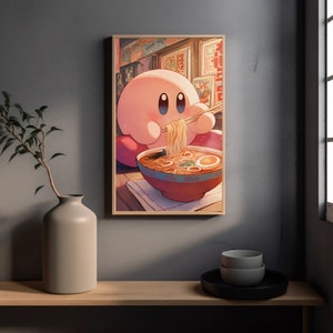 May include: A framed print featuring a pink cartoon character eating ramen noodles with chopsticks. The character is in front of a red bowl filled with noodles, broth, and an egg. The background shows Japanese-style storefronts.