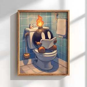 Op de afbeelding: Een ingelijste prent met een cartoon bom-personage met een brandende lont, zittend op een toilet en lezend. De badkameromgeving omvat een toilet, een handdoekenrek en blauwe betegelde muren. Het kunstwerk heeft een humoristisch thema.
