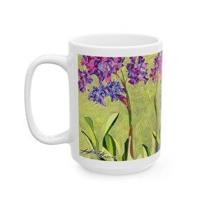 Pode incluir: Caneca de cerâmica branca com um design floral de jacintos roxos e azuis sobre um fundo verde. A caneca tem uma alça grande e um acabamento brilhante, ideal para café.