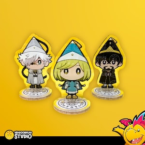 May include: Three acrylic character standees featuring chibi-style figures with pointed hats. The left figure has white hair, the center figure has blonde hair, and the right figure has dark hair and a mustache. Each stands on a circular base with symbols.