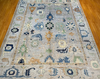 May include: A light gray rug with a blue, green, and beige floral pattern. The rug has a border with a repeating design.