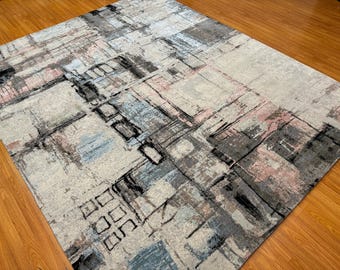 May include: Abstract area rug with a geometric pattern in shades of gray, blue, and pink. The rug has a distressed, vintage look.