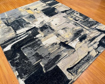 May include: Abstract area rug with a modern design featuring shades of gray, black, and beige. The rug has a textured, hand-woven look.