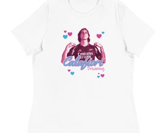 May include: White t-shirt with a graphic of a person in a dark jersey. The graphic includes the text "Calafiori Dreaming" in pink and blue, with pink and blue hearts scattered around.