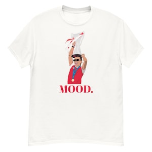 Könnte beinhalten: Weißes T-Shirt mit einer Grafik einer Person mit Sonnenbrille und roter Weste, die eine Trophäe hält. Das Wort "MOOD." ist rot unter der Grafik aufgedruckt. Ein lässiges, sportliches Design.