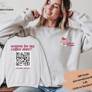 Könnte beinhalten: Ein hellgraues Sweatshirt mit dem Text "wanna be my coffee date?" und einem QR-Code auf der Rückseite. Auf der Vorderseite befindet sich eine Cartoon-Kaffeetasse mit den Worten "you, me & coffee". Das Sweatshirt ist von Pure Vibes Studio.