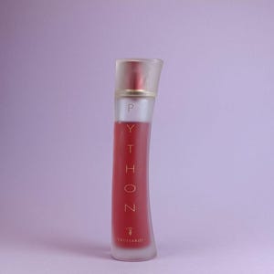 Op de afbeelding: Een rode en transparante parfumfles met het woord "PYTHON" verticaal afgedrukt. De fles heeft een transparante, schuine dop en een rode vloeistof binnenin. De merknaam "Trussardi" staat onderaan.
