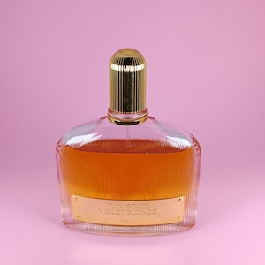 Op de afbeelding: Een doorzichtige glazen fles Tom Ford Violet Blonde parfum met een gouden dop en etiket. De fles heeft een getextureerd oppervlak en is gevuld met een licht amberkleurige vloeistof.