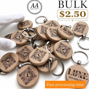 May include: A collection of round wooden keychains featuring laser-engraved QR codes and text including LUXE AESTHETIC STUDIO and 954-868-0044. The keychains are attached to silver-toned metal split rings. The image includes text reading BULK $2.50.