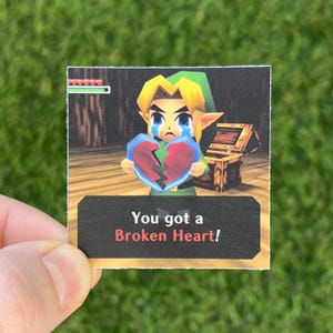 Puede incluir: Un personaje de videojuego, Link de The Legend of Zelda: Ocarina of Time, sostiene un corazón roto y llora. El texto en la imagen dice "You got a Broken Heart!"