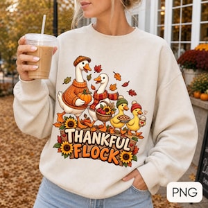 Peut inclure: Un sweat-shirt à col rond couleur crème orné d'un motif représentant quatre oies vêtues de vêtements d'automne, notamment des bonnets et des écharpes. Les oies sont entourées de feuilles d'automne, de tournesols et d'un panier de pommes.