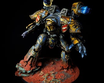 Peut inclure: Maquette détaillée d'une machine de guerre, aux couleurs bleu, or et rouge. Le modèle repose sur une base texturée brun-rouge. Le design comprend des détails complexes et des armes. Le texte "FERRAX RUPTOR" est visible sur la base.