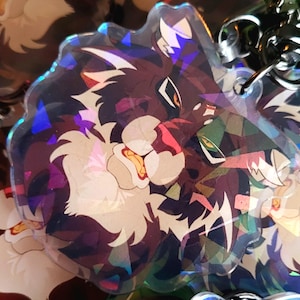 Op de afbeelding: Een holografische charme met een cartoonwolf met bruine vacht, witte markeringen en groene ogen. De charme is iriserend en heeft een regenboog effect.