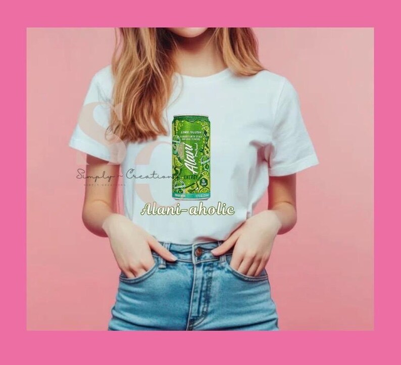 May include: A white t-shirt with a green and white Alani Nu Lime Flush energy drink can graphic. The text "Alani-aholic" is below the can. The model is wearing blue jeans.
