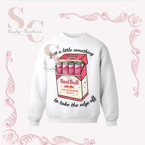 May include: White sweatshirt featuring a graphic of a Red Bull The Summer Peach box with cans. Text on the sweatshirt reads "Just a little something to take the edge off."