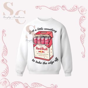 May include: White sweatshirt with a graphic of a Red Bull box containing six cans. The box is red and white with the text "Red Bull The Peach Edition White Peach" and the phrase "Just a little something to take the edge off."