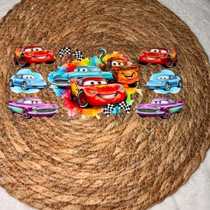 May include: A selection of car-shaped stickers, inspired by the film "Cars." The stickers showcase various car designs in red, blue, orange, and purple, with checkered flag details. They are arranged on a woven, circular placemat, providing a vibrant display.
