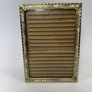 Op de afbeelding: Een rechthoekige fotolijst met een goudkleurige metalen rand met een gedraaide, touwachtige textuur en decoratieve hoekaccenten. De lijst bevat een lichtbruin, horizontaal geribbeld kartonnen inzetstuk in het weergavegebied.