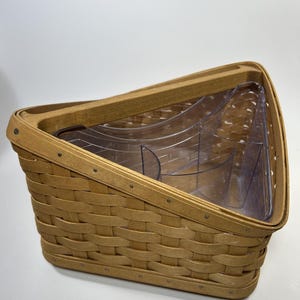 Puede incluir: Una cesta trenzada triangular con acabado marrón claro y un inserto de plástico transparente con múltiples compartimentos. La cesta tiene un borde superior inclinado y un marco de madera resistente, ofreciendo una solución de almacenamiento estructurada.