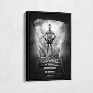 May include: Black and white framed print featuring a muscular person standing on steps with a cloudy background. The print includes the text "Losers focus on winners. Winners focus on winning." and the name "Conor McGregor."