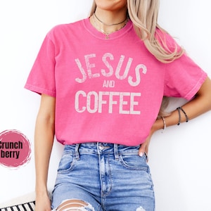 May include: A bright pink t-shirt with the words "JESUS and COFFEE" printed in a distressed white font. The shirt is paired with blue denim jeans. The image also includes a "Crunch berry" color swatch.