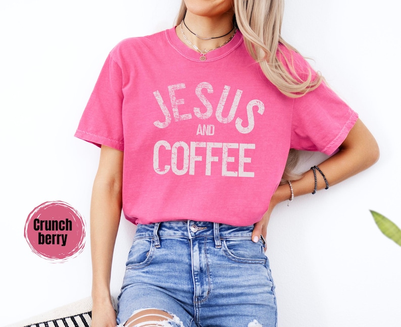 May include: A bright pink t-shirt with the words "JESUS and COFFEE" printed in a distressed white font. The shirt is paired with blue denim jeans. The image also includes a "Crunch berry" color swatch.
